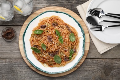 Photo of Delicious pasta with anchovies, tomato sauce and basil on wooden table, flat lay