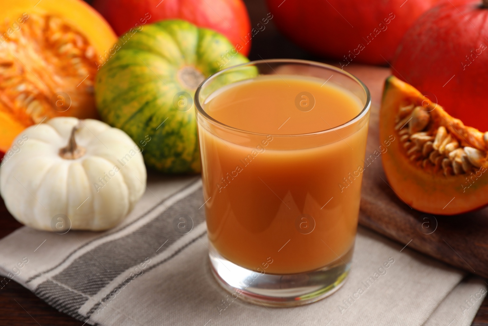 Photo of Tasty pumpkin juice in glass and different pumpkins on wooden table