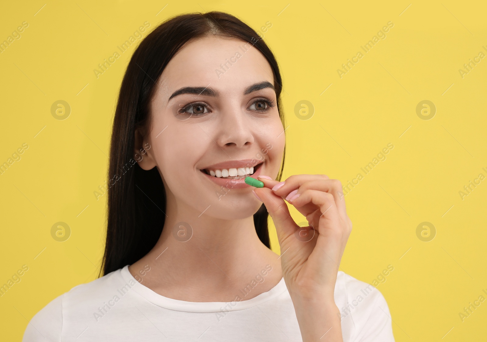 Photo of Young woman taking vitamin capsule on yellow background