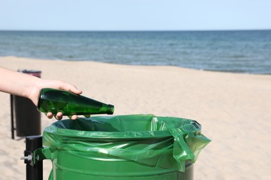Woman throwing glass bottle in bin on beach, closeup. Recycling concept
