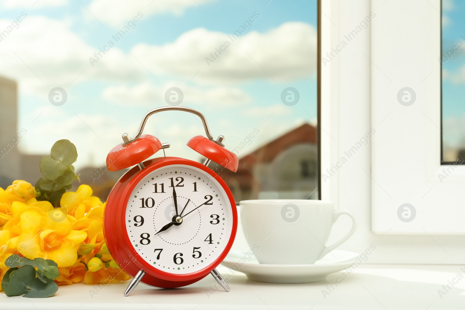 Photo of Alarm clock, beautiful yellow freesias and cup of drink on windowsill. Good morning