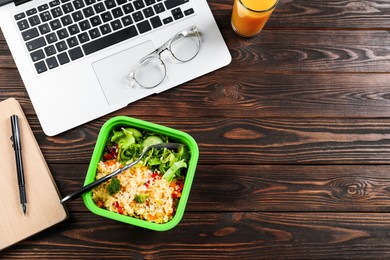 Photo of Containertasty food, fork, laptop, glass of juice, and notebook on wooden table, flat lay with space for text. Business lunch