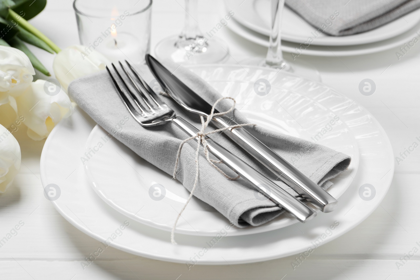 Photo of Stylish setting with cutlery, burning candle and tulips on white wooden table