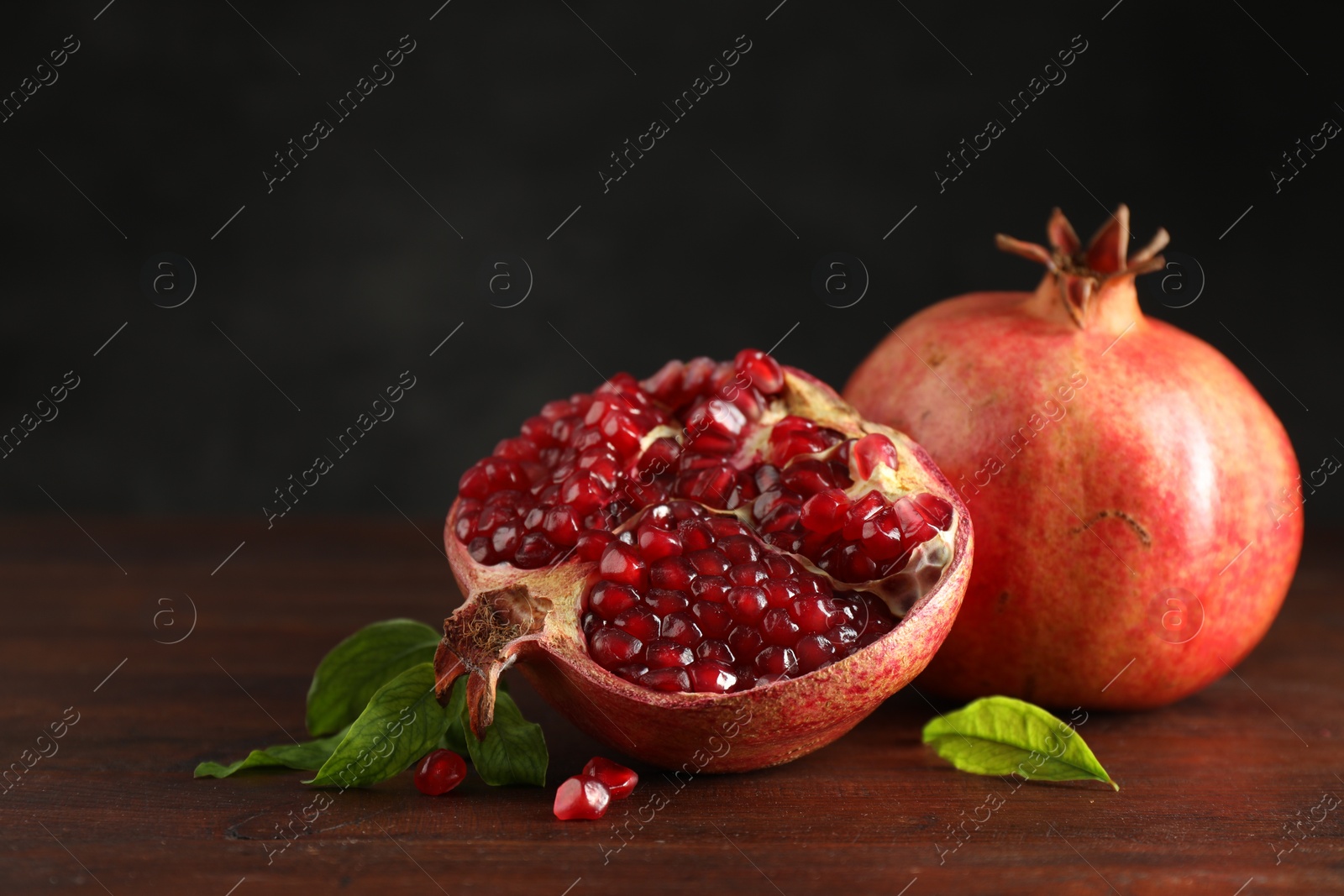 Photo of Fresh pomegranates and green leaves on wooden table, space for text