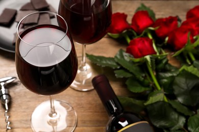 Photo of Glass of red wine near beautiful roses on wooden table, closeup