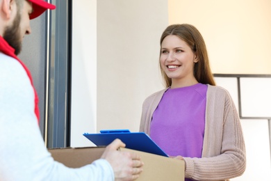 Photo of Woman receiving parcel from delivery service courier indoors
