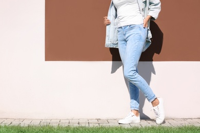 Photo of Young hipster woman in stylish jeans and jacket posing near color wall