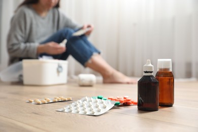 Photo of Woman with first aid kit sitting on floor indoors, focus on medicaments