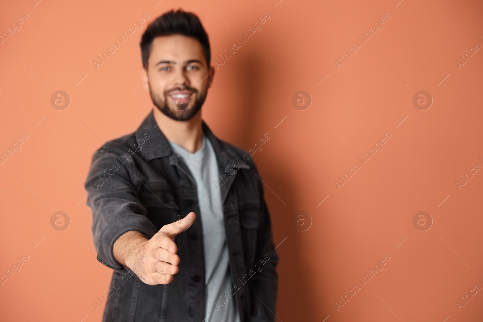 Photo of Man offering handshake against peach background, focus on hand. Space for text