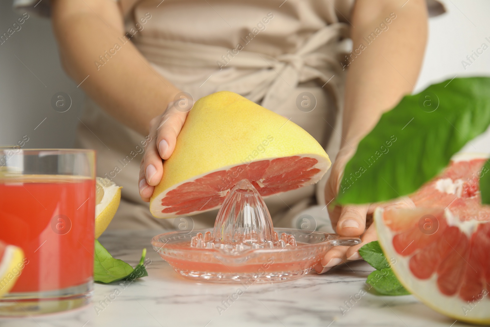 Photo of Woman squeezing pink pomelo juice at white marble table, closeup