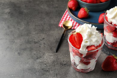 Photo of Delicious strawberries with whipped cream served on grey table. Space for text
