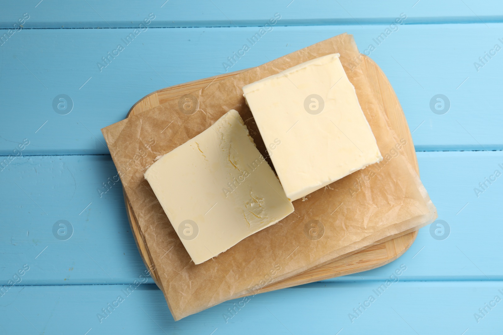 Photo of Block of tasty butter on light blue wooden table, top view