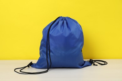 Photo of Blue drawstring bag on white wooden table against yellow background