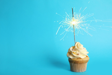 Image of Birthday cupcake with sparkler on light blue background. Space for text
