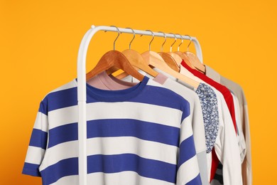 Rack with stylish women's clothes on wooden hangers against orange background