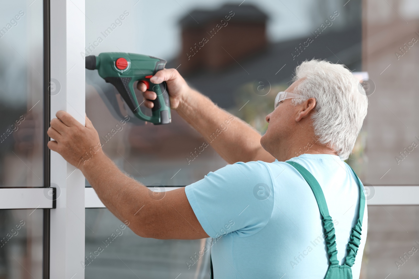 Photo of Mature construction worker repairing plastic window with electric screwdriver indoors