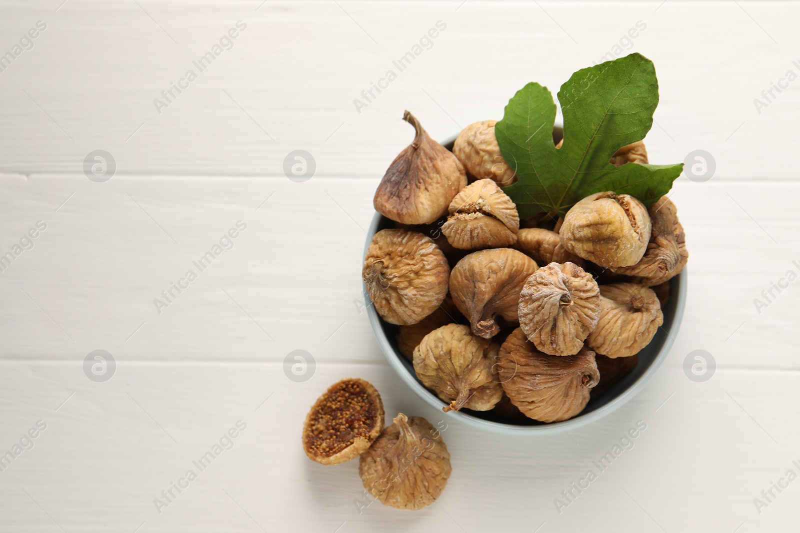 Photo of Bowl with tasty dried figs and green leaf on white wooden table, flat lay. Space for text