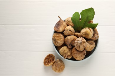 Bowl with tasty dried figs and green leaf on white wooden table, flat lay. Space for text