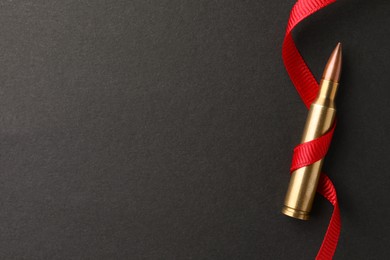 Photo of Bullet and red ribbon on black background, top view. Space for text