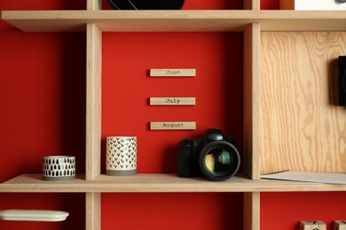Photo of Stylish wooden shelf with camera and decorative elements on red wall