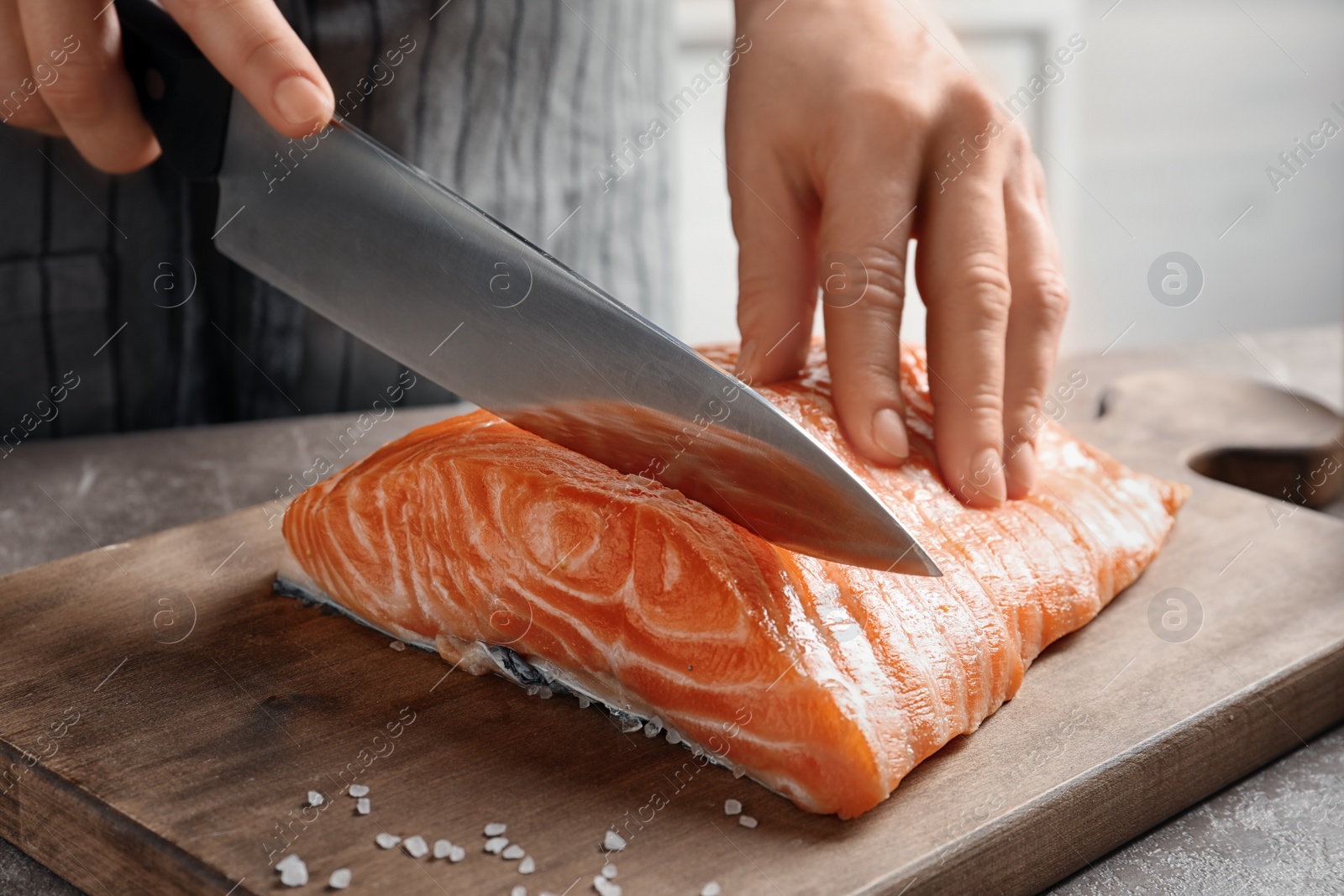 Photo of Woman cutting raw salmon fillet on wooden board