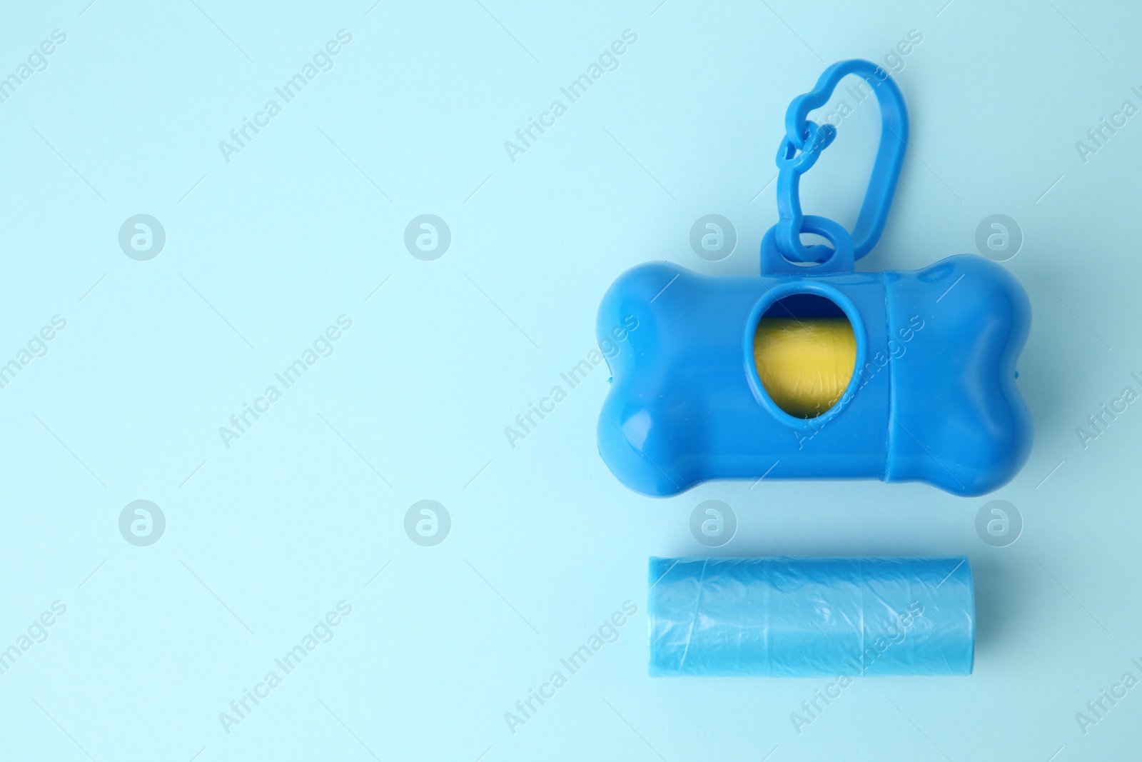 Photo of Dog waste bags and dispenser on light blue background, flat lay. Space for text