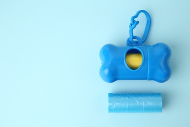 Photo of Dog waste bags and dispenser on light blue background, flat lay. Space for text