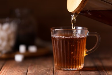 Photo of Pouring delicious tea into glass cup on wooden table, closeup. Space for text