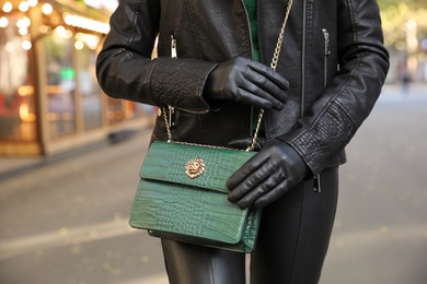 Photo of Woman with leather gloves and stylish green bag on city street, closeup