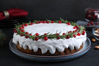 Traditional Christmas cake decorated with rosemary and cranberries on dark grey table, closeup