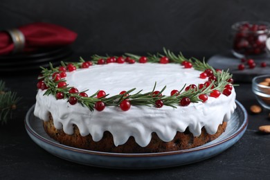 Photo of Traditional Christmas cake decorated with rosemary and cranberries on dark grey table, closeup