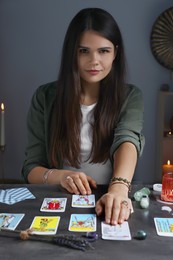 Photo of Fortune teller predicting future on spread of tarot cards at grey table indoors