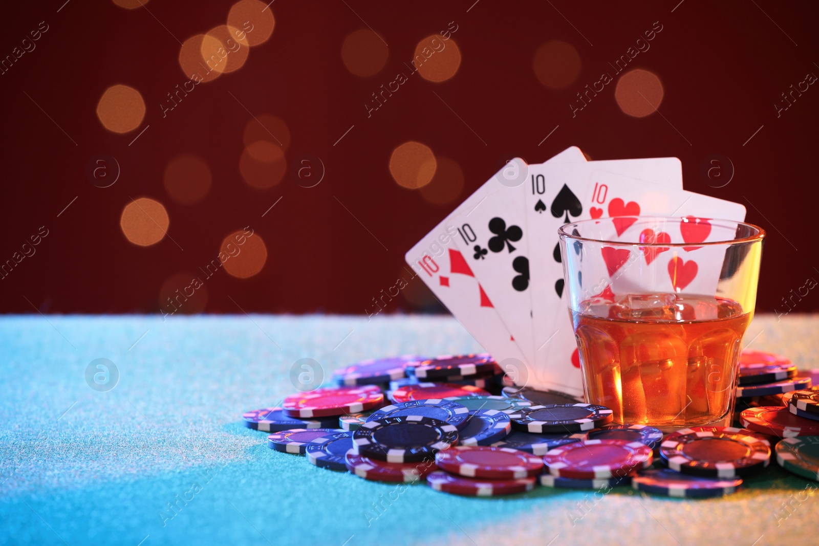 Photo of Alcohol drink, playing cards and casino chips on table against blurred lights. Four of a kind poker combination