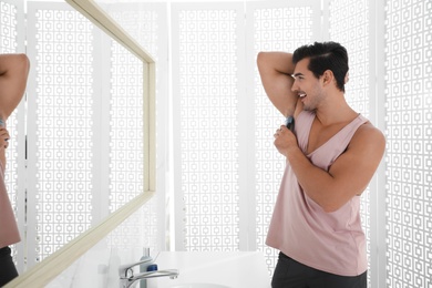 Photo of Handsome young man applying deodorant in bathroom