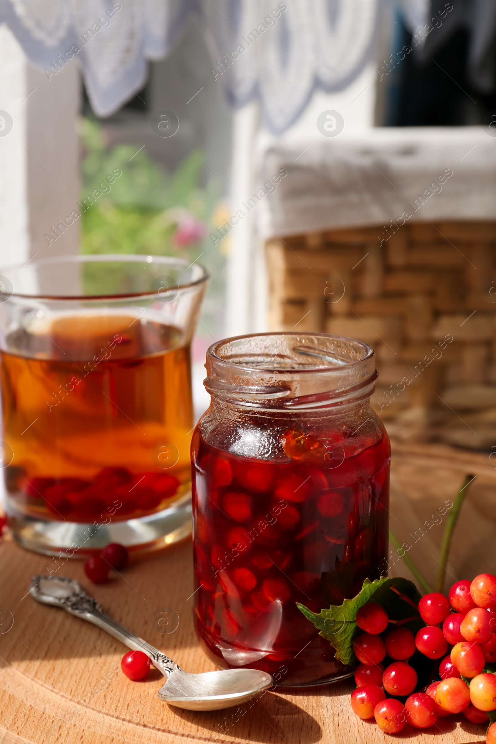 Photo of Tasty hot drink, jam and viburnum berries on wooden board indoors