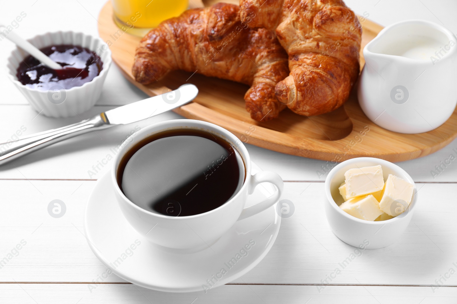 Photo of Fresh croissants, butter, jam and coffee on white wooden table. Tasty breakfast