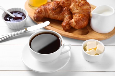 Photo of Fresh croissants, butter, jam and coffee on white wooden table. Tasty breakfast