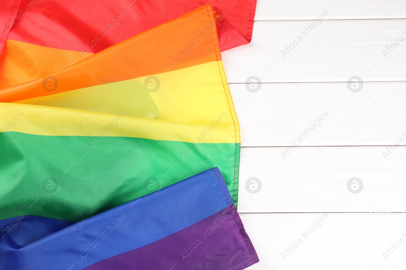 Photo of Rainbow LGBT flag on white wooden table, top view. Space for text