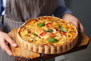 Photo of Woman holding board with tasty quiche indoors, closeup