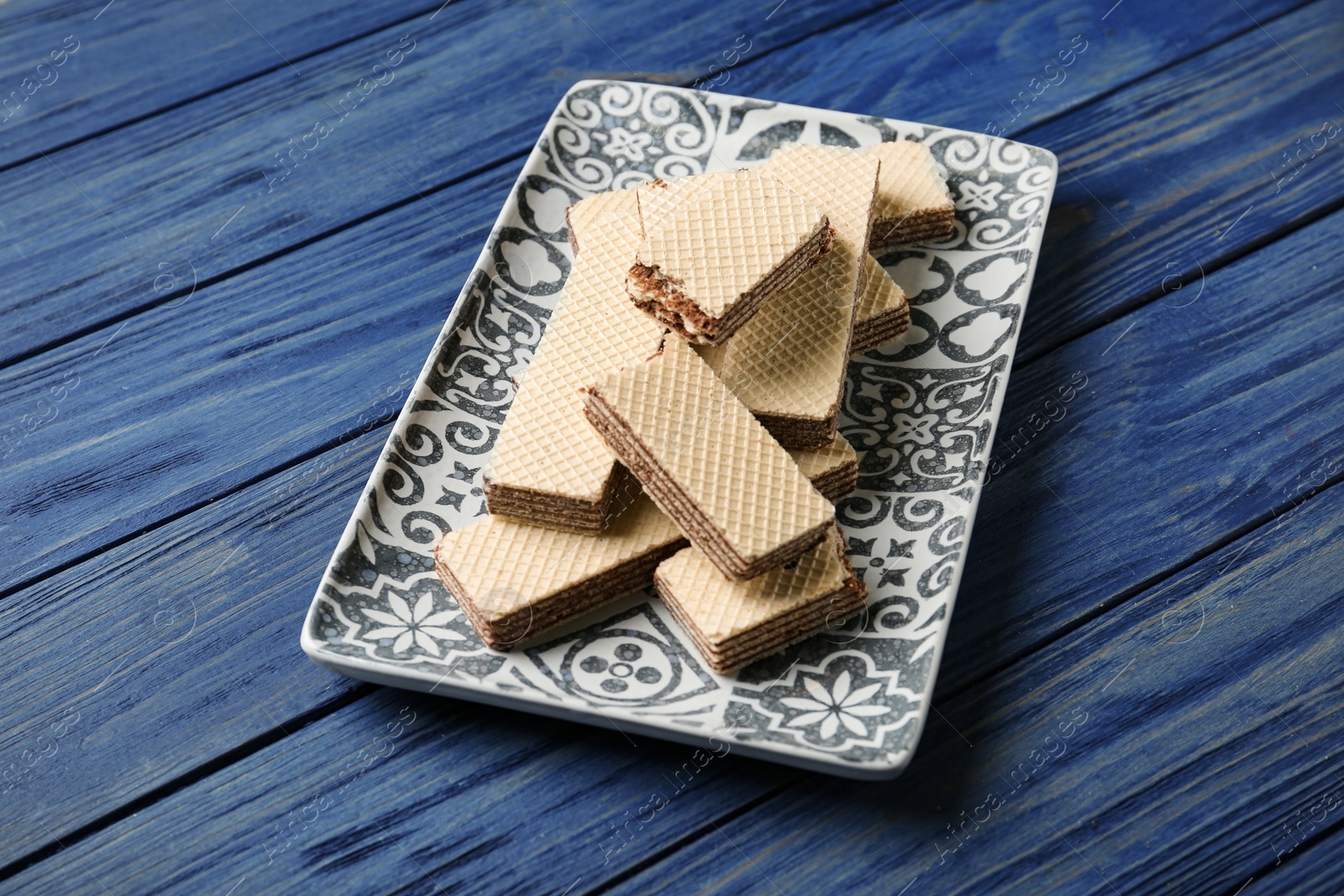 Photo of Plate of delicious crispy wafers with chocolate filling on blue wooden table