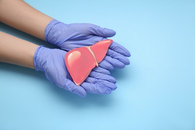 Photo of Doctor in gloves holding paper liver on light blue background, closeup and space for text. Hepatitis treatment