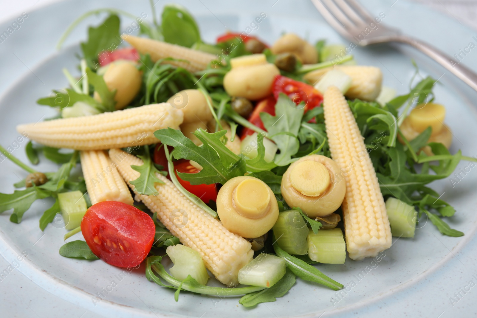 Photo of Tasty baby corn with vegetables, arugula and mushrooms on plate, closeup