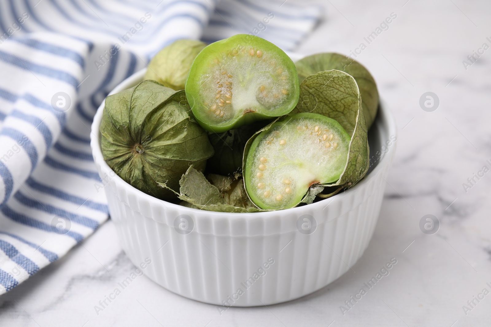 Photo of Fresh green tomatillos with husk in bowl on light marble table, closeup