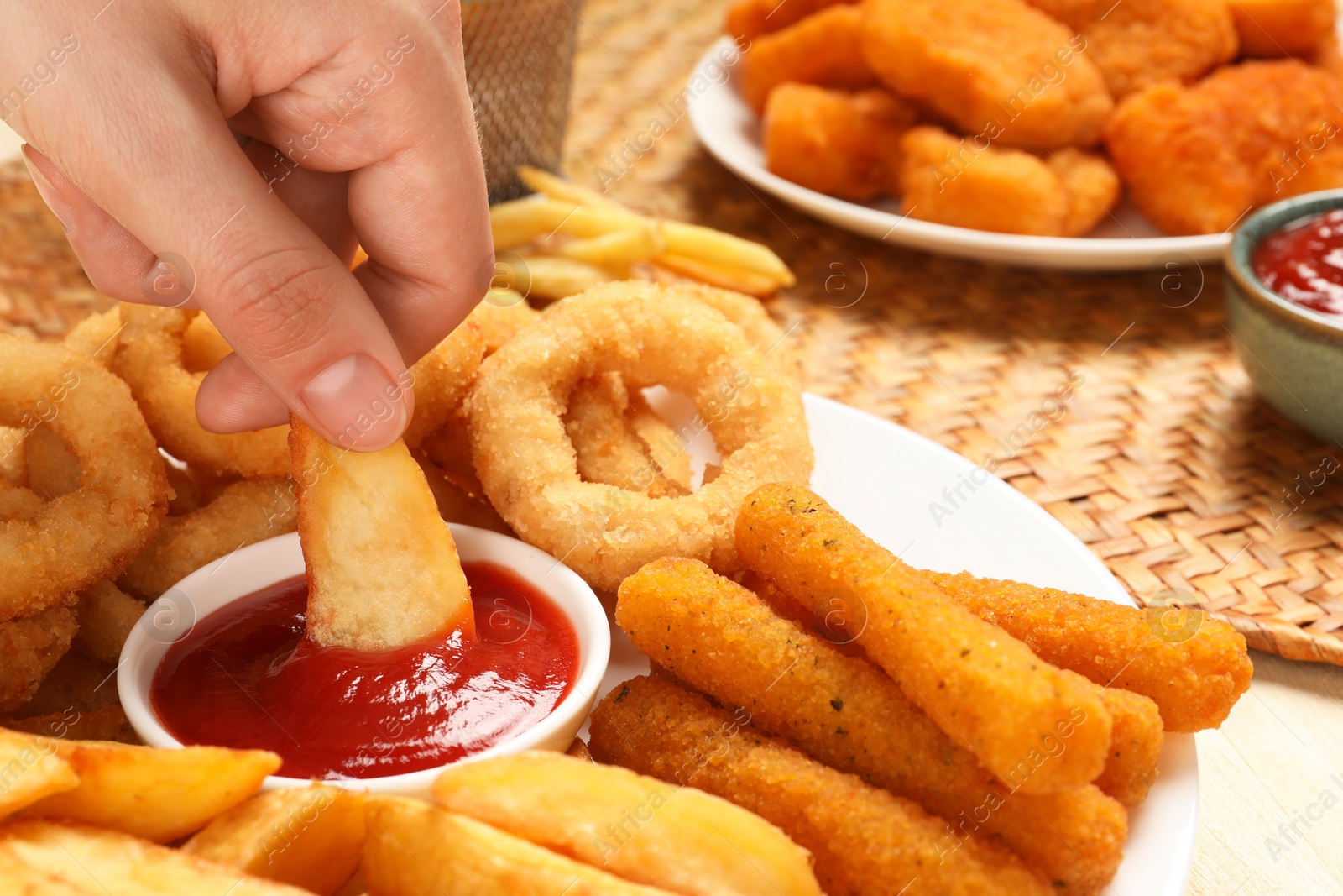 Photo of Woman dipping baked potato into bowl with tasty ketchup at table, closeup