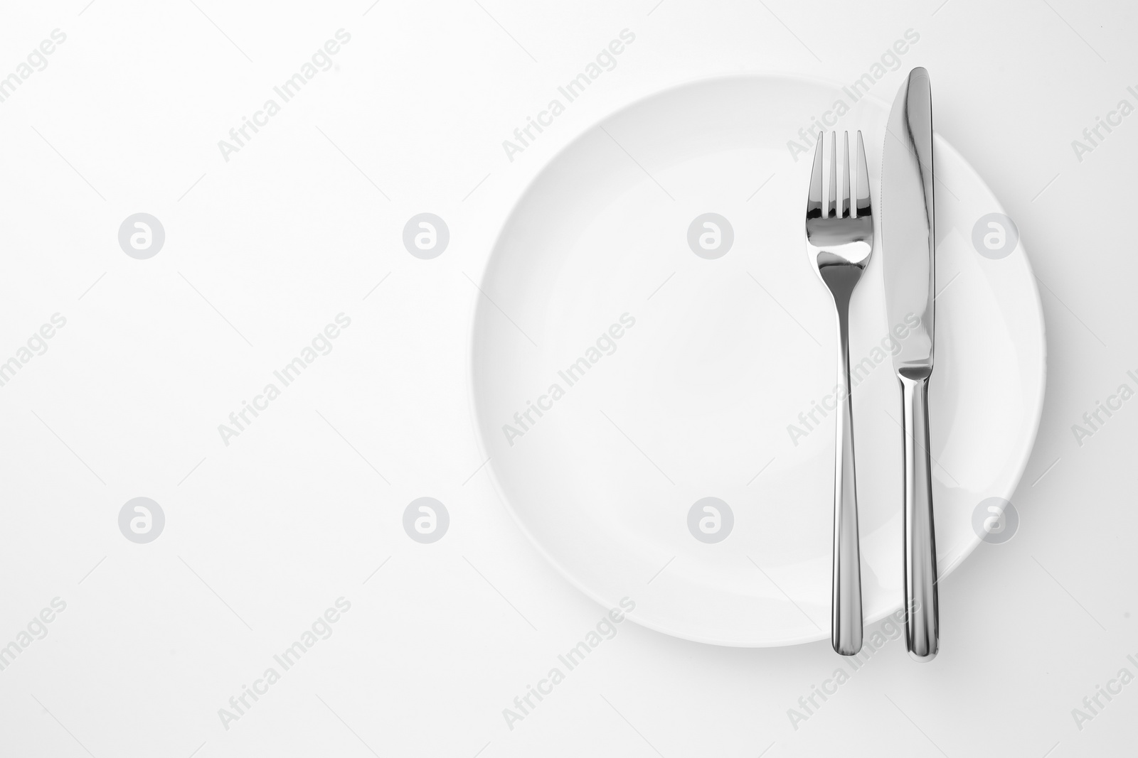 Photo of Plate, fork and knife on white background, top view. Space for text