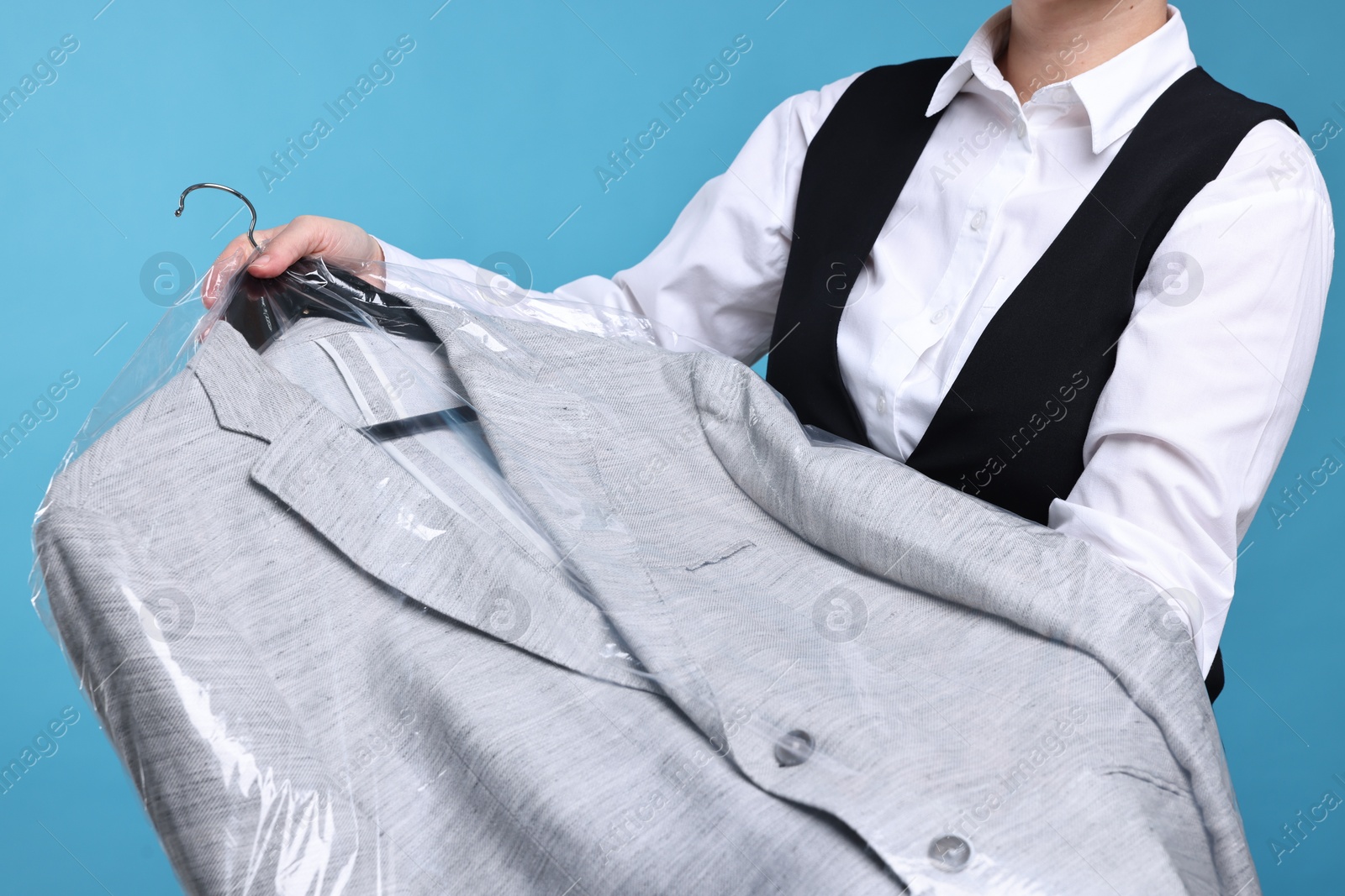 Photo of Dry-cleaning service. Woman holding jacket in plastic bag on light blue background, closeup