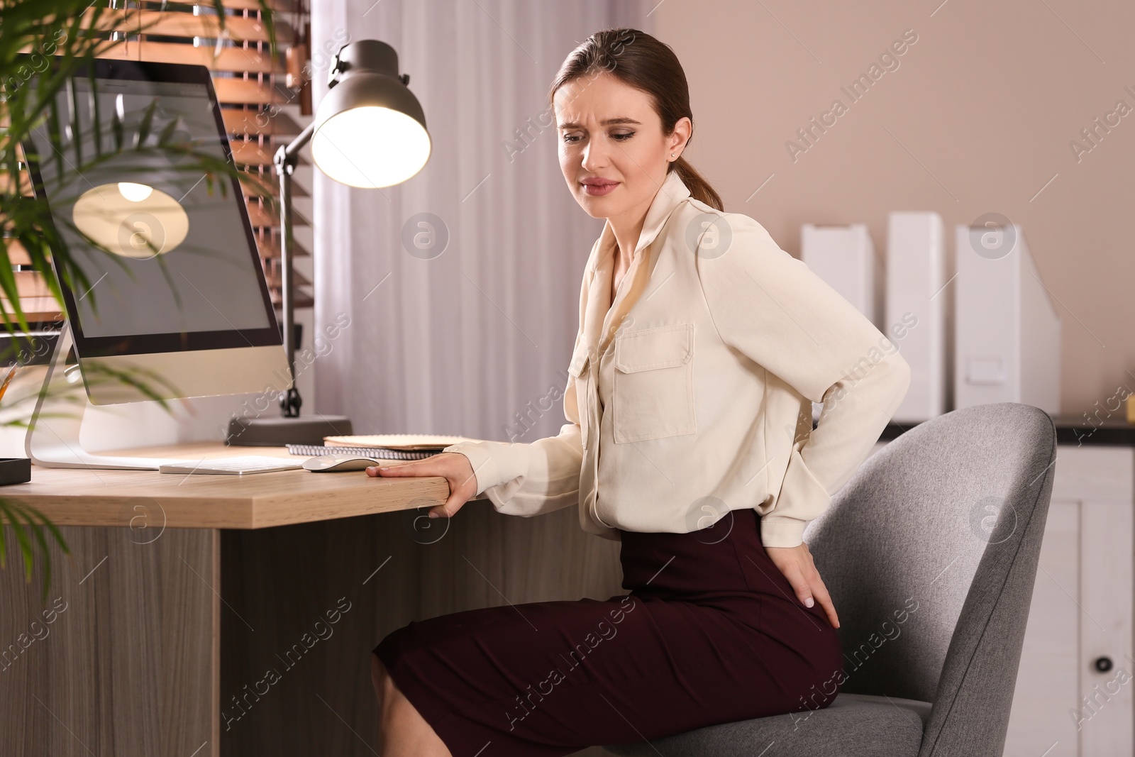 Photo of Young woman suffering from hemorrhoid at workplace in office