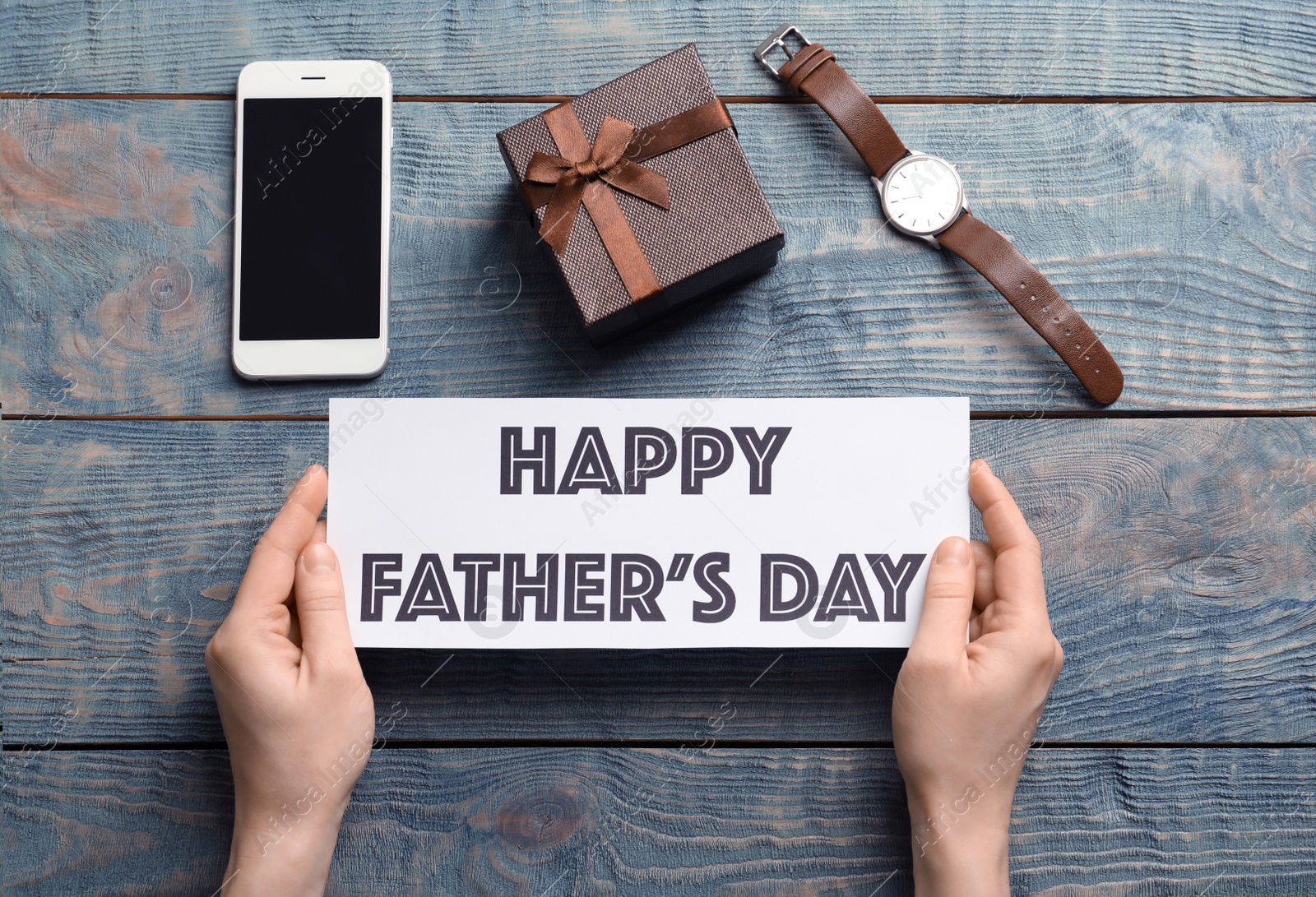 Photo of Man holding card with words HAPPY FATHER'S DAY over table with gifts, top view