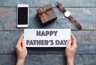 Man holding card with words HAPPY FATHER'S DAY over table with gifts, top view