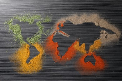 World map of different spices on black wooden table, flat lay